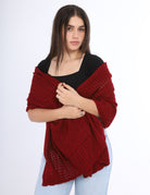 Woman wearing a red knitted shawl over a black top on a white background